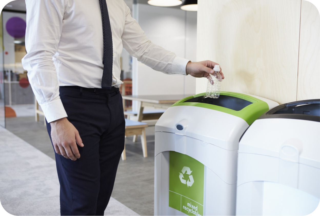 Person placing a plastic bottle into a recycling bin in a modern office space.
