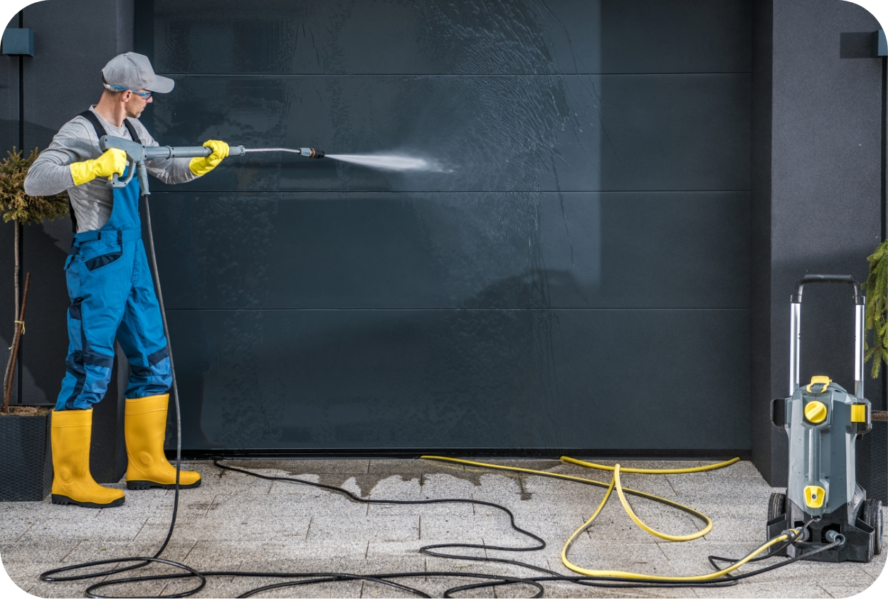 Pressure washing exterior wall with a high-pressure cleaner and safety gear.